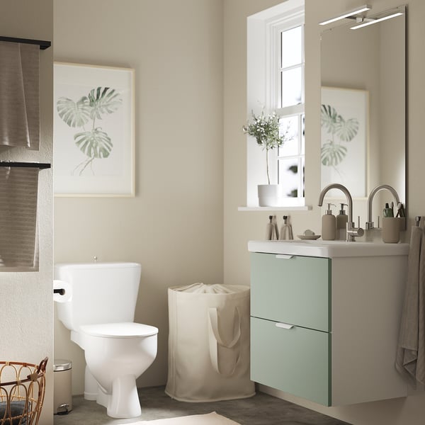 Mint-green cabinet, white sink, mirror, toilet, laundry bag, art.