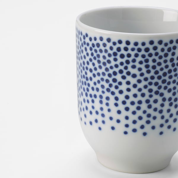 Porcelain cup with white and blue dotted pattern, smooth rim, and glossy finish. Elegant and detailed design.