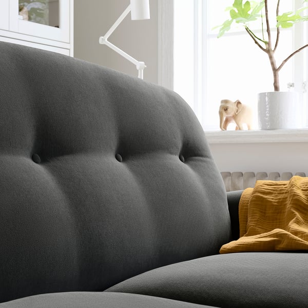 Modern dark grey sofa, soft chenille material, high backrest, round armrests, plush cushions, near window with plant and decor.