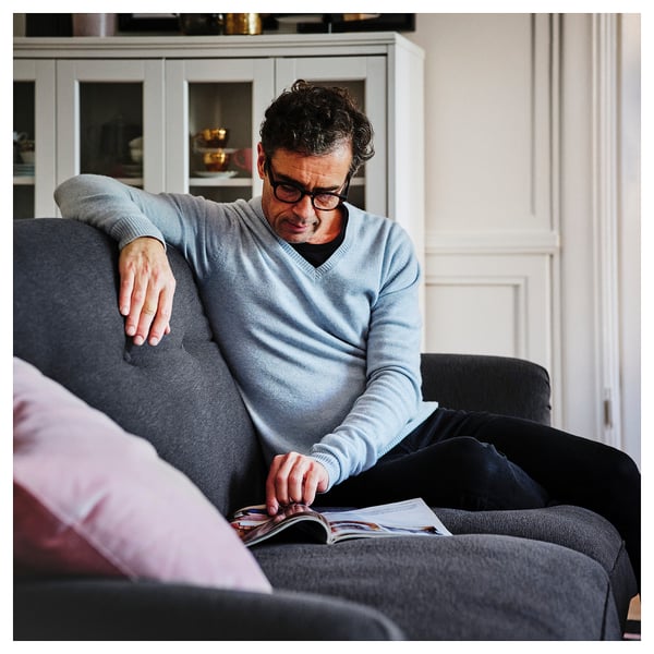 Person in light blue sweater reads magazine on soft grey ESSEBODA sofa, pink cushion.