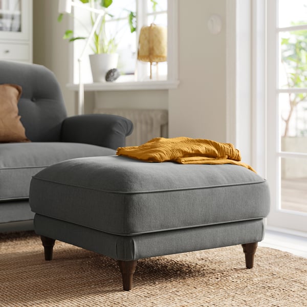 Grey ESSEBODA ottoman, mustard throw, next to dark blue sofa, cosy living area.