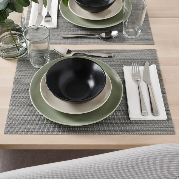 Table set with FÄRGKLAR bowls, plates, cutlery, and glasses on place mats, ready for dining.