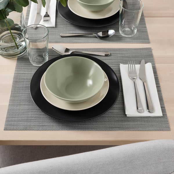 Table set with FÄRGKLAR green bowl, white plate, cutlery, glass on woven placemat.