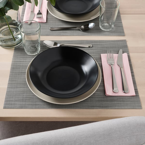 Two table settings each with a grey placemat, black bowl, spoon, fork, knife, napkin, and glass.