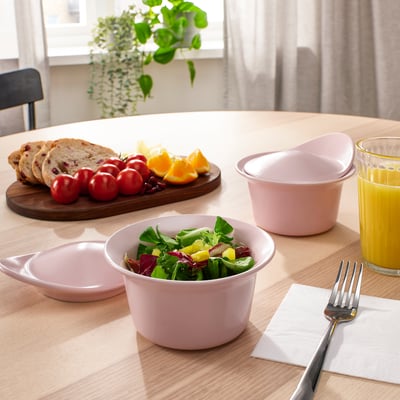 Pink bowls with salad, empty bowl, fruit, bread, oj, fork on napkin.