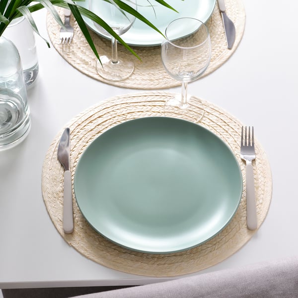 Two place settings with FÄRGKLAR green plates, silverware, glasses, and woven placemats on a white tablecloth.