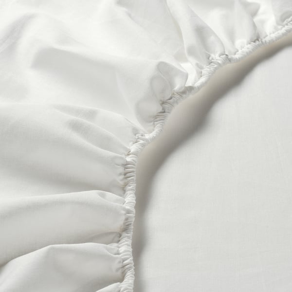 Close-up of crisp, white, high-quality cotton fitted sheet with elastic edges for secure fit. Smooth, even weave visible.