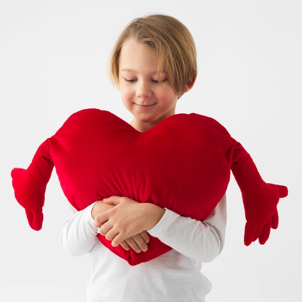 A girl hugs a large red heart-shaped pillow. It symbolises love and makes a great gift.