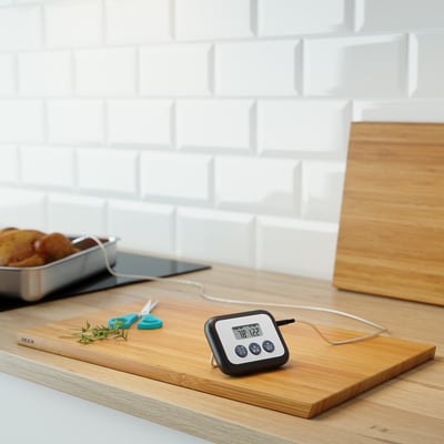 Kitchen thermometer on cutting board; digital display with cord, cooking timer, temperature probe.