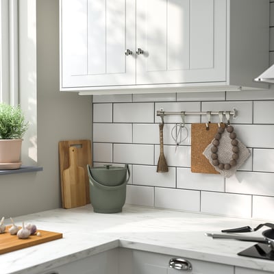 Kitchen counter with tiled backsplash, green bin, cutting board, plant, hanging tools, garlic, and knife set.