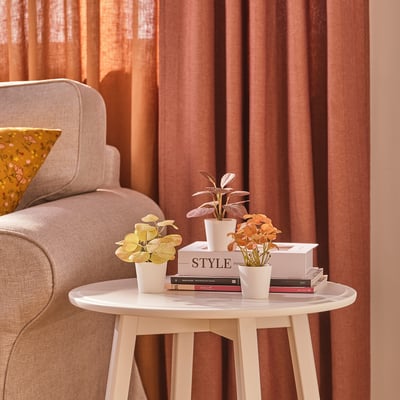 Small white table holds three potted artificial plants and books, ideal for indoor and outdoor use.