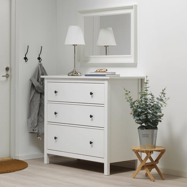 Modern entryway with white chest, table lamp, mirror, and FEJKA plant.