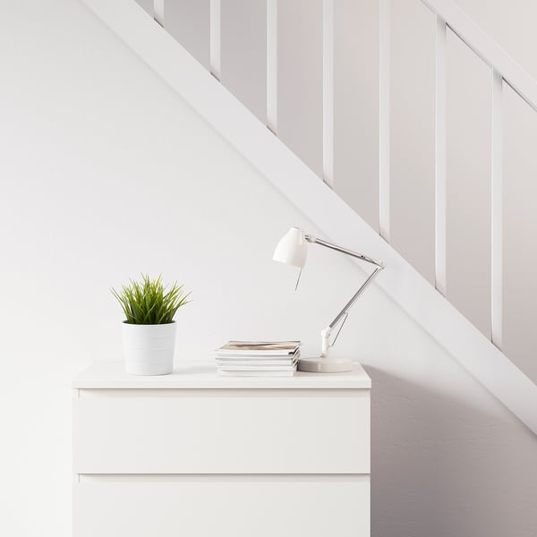 White desk with lamp, stack of books, and a potted FEJKA plant.