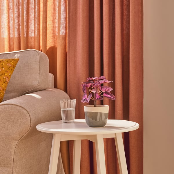 White side table with potted plant and glass in living room.