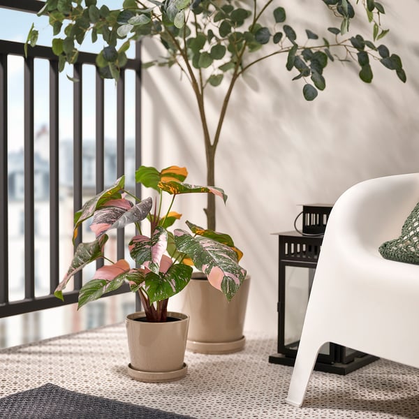 Balcony with FEJKA plant, white chair, black lantern, city view.