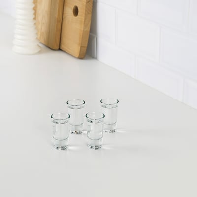 Four clear glasses on white counter, wooden cutting board behind.