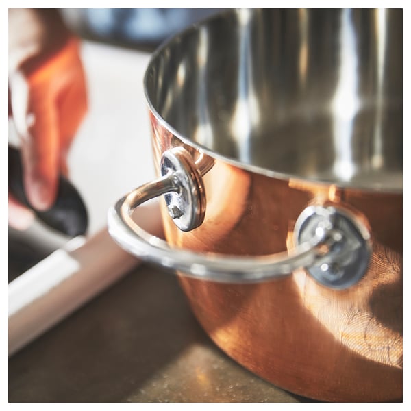 Copper cookware with steel handle, lid on counter.