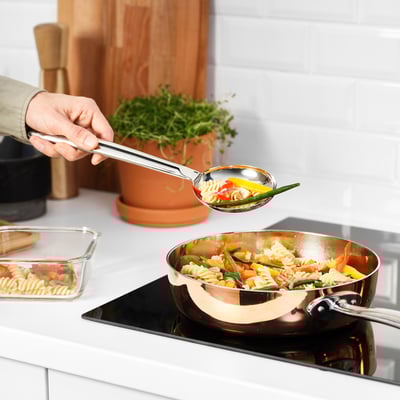 A person loads a FINMAT spoon with stir-fried noodles and vegetables, showcasing its deep bowl and sturdy handle designed for stirring and serving.