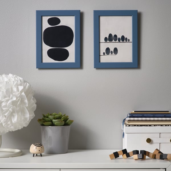 Two blue art prints on grey wall above shelf with plants and books.
