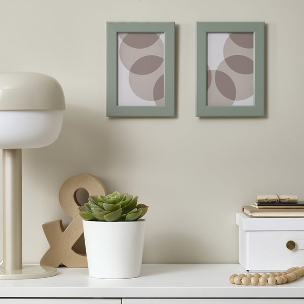 Green frames with abstract art, white lamp, succulent, books, beads.