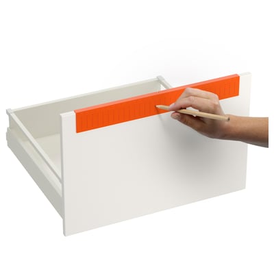 Person using orange drill template to mark position on white drawer for precise handle placement.