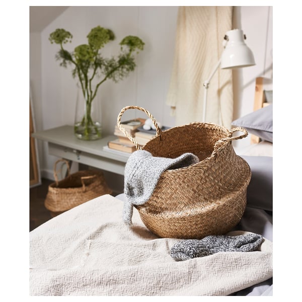 Seagrass basket with sweater on bed, flowers nearby.
