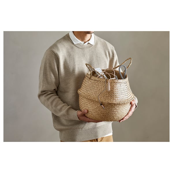 Person holding woven seagrass basket. Neutral beige tones, handles can be turned up or down.