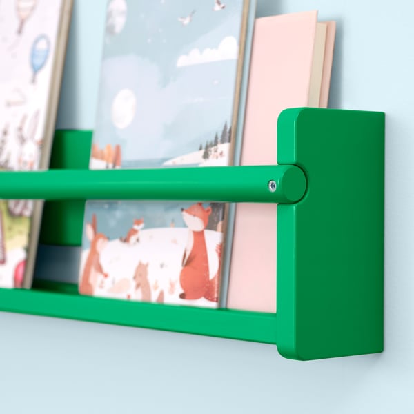Green wooden shelf mounted on light blue wall with a colourfully illustrated book and a pink book standing upright.