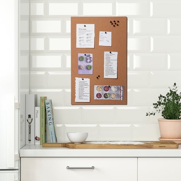 Kitchen memo board with notes, photos, and pins on cork, mounted on tiled wall.
