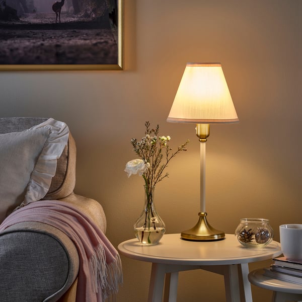 Cozy living room with beige FLYGHÖJD lamp, small round table, grey chair, and vase with flowers.