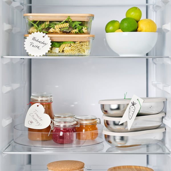 Open fridge with labelled containers, jars, and fruit. Labels help identify contents.