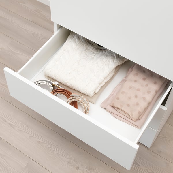 White wardrobe drawer, neatly folded towels, belts, and accessories stored inside.