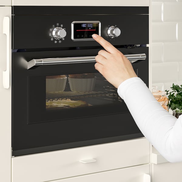 Person adjusting black FORNEBY oven settings in modern kitchen. Digital display shows 180° c. Control panel with preset programmes.