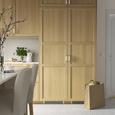 Modern kitchen with light wood FORSNÄS fridge, chair, vase, teapot, and groceries.