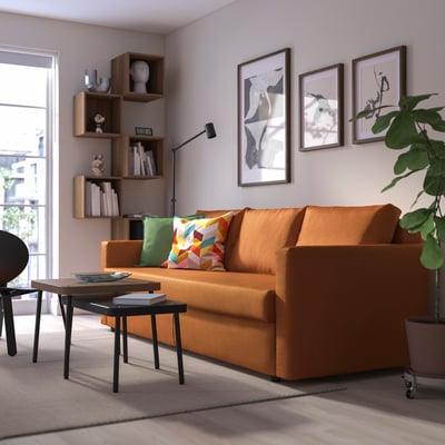 A cosy living room with a bright orange FRIHETEN sofa, a modern coffee table, and a bookshelf filled with books.