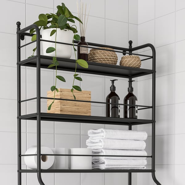 Black metal over-the-toilet shelf with three tiers storing towels, toiletries, and plants.