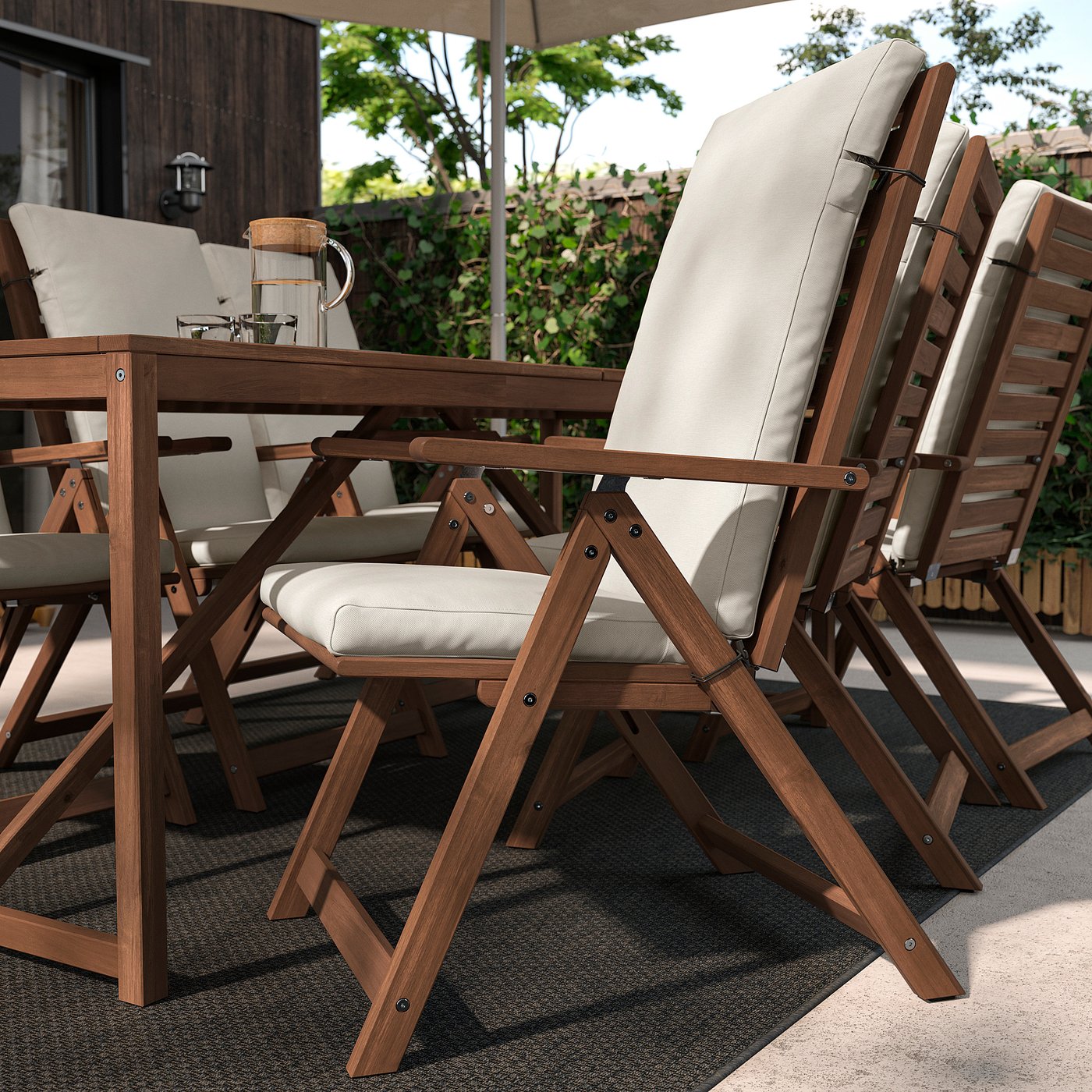 Outdoor patio set with FRÖSÖN/DUVHOLMEN light grey cushioned wooden chairs on black rug.
