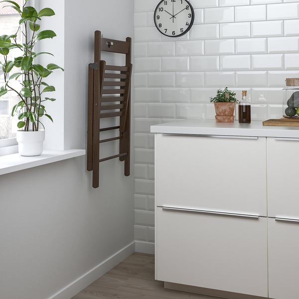 Kitchen corner with wooden step ladder, wall clock, potted plants, and white cabinets. The ladder has a seat hole for wall storage.