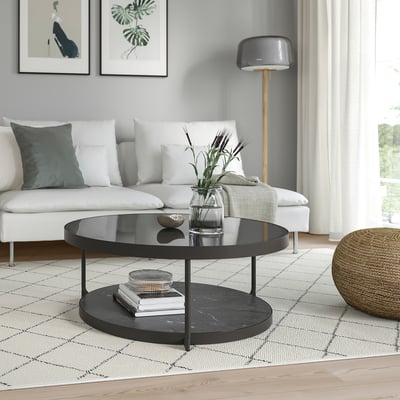 Modern living room with black coffee table, glass top, white couch, lamp, and decor on patterned rug.