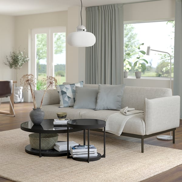 Modern living room with gray fabric sofa, black round side table, blue throw pillows, large window, and blue curtains.