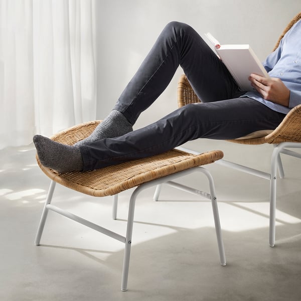 Person reclining in a wicker chair, reading a book, with feet resting on a matching footstool.