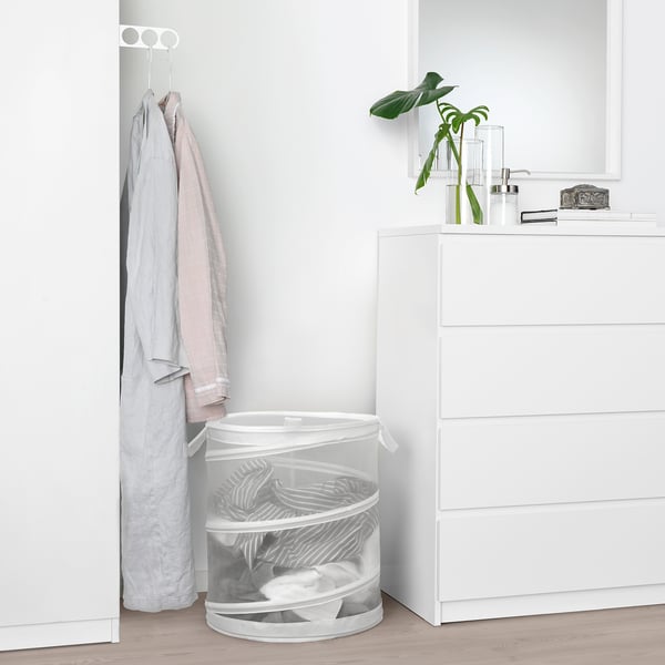 White FYLLEN laundry basket between dresser and clothes rack with folded clothes.