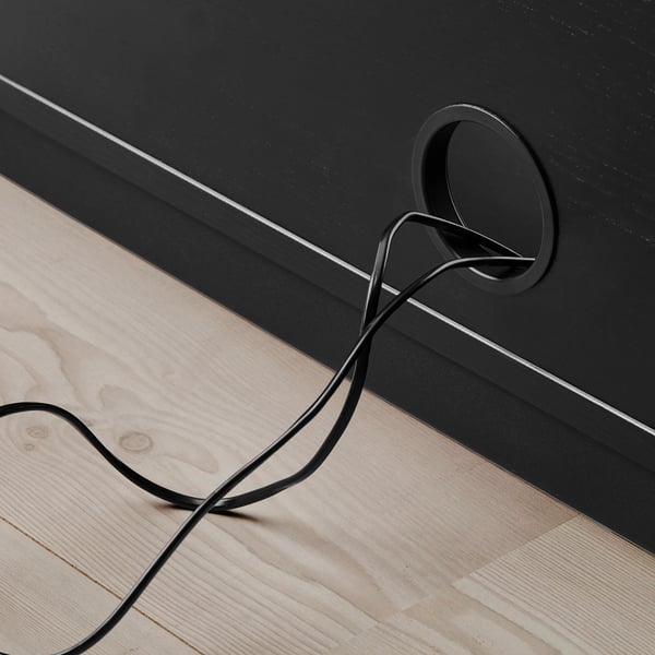 Black cable exits round hole in dark wooden furniture, showing cable management feature.