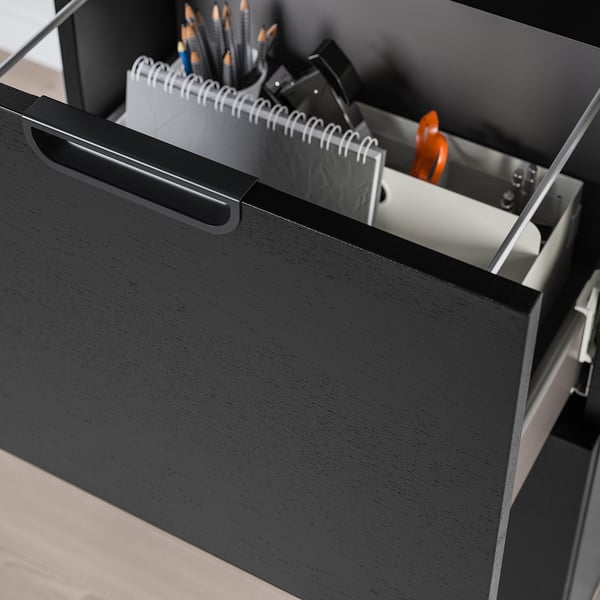 Black office drawer open, revealing supplies like notepads, pencils, and an orange folder.