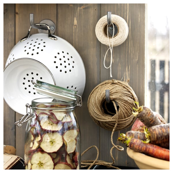 A wooden wall mounts multiple kitchen tools: a white colander, string spool, and jar filled with dried apple slices.