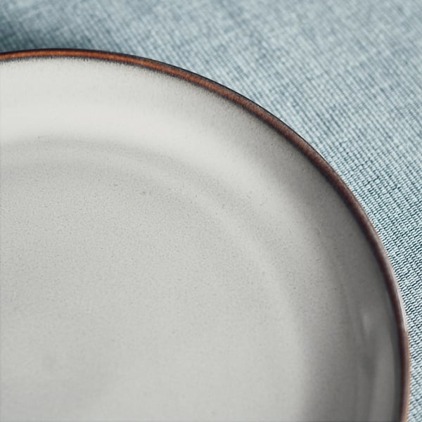 A white, smooth, round dish with a dark rim on a blue tablecloth.