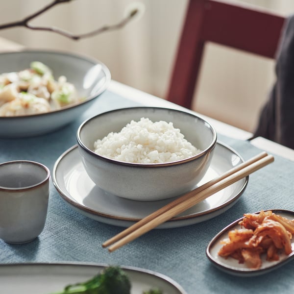 Blue table setting with GLADELIG bowl of rice, chopsticks, side dish, and small cup.