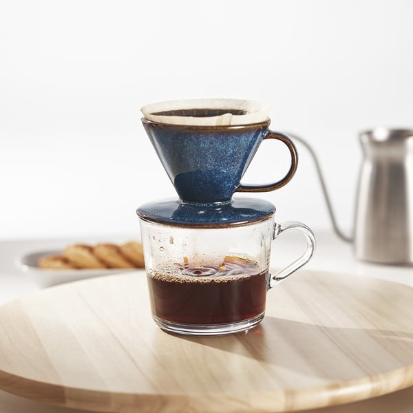 A clear glass mug filled with coffee brewed using a blue ceramic pour-over philtre holder, placed on a wooden table.