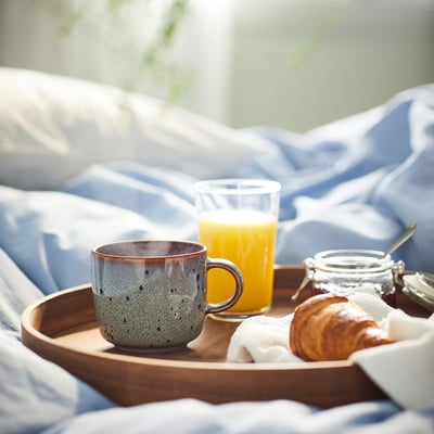 Breakfast tray with GLADELIG mug, orange juice, pastry, jam. Mug is blue, large, ceramic with dotted design.
