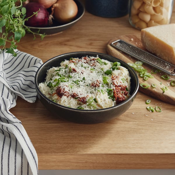 Bowl of creamy dish with cheese, tomatoes, and onions on table.